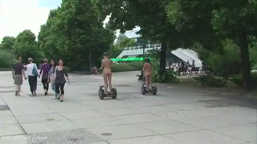 Two Girls Walk Naked Down The Street Riding A Skateboard