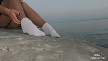 Amazing Mistress legs in sexy pantyhose with white socks on the evening wild seashore.