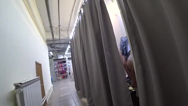Voyeur in a public shopping center peeps into the changing room for a girl with a